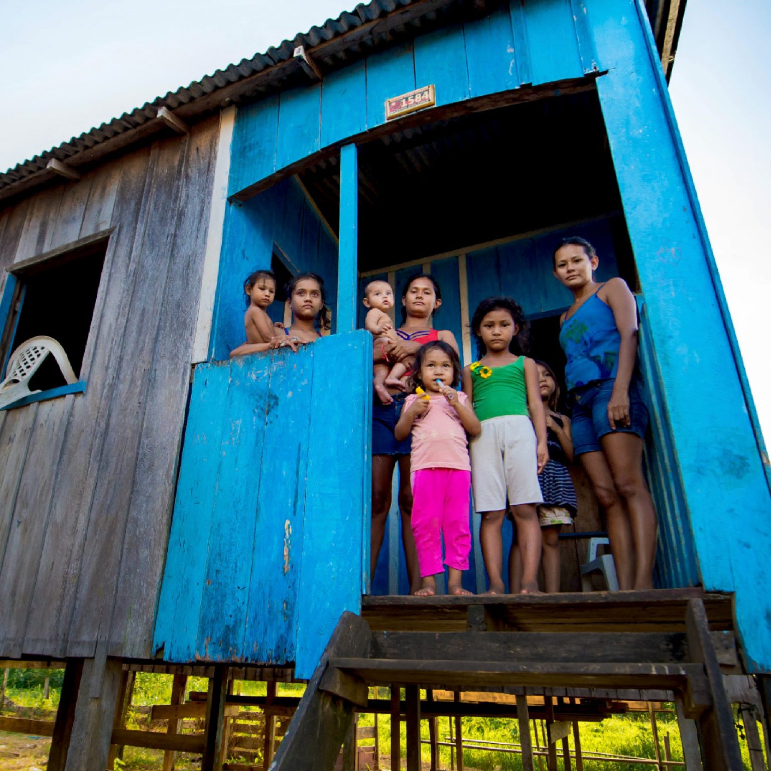 Família na porta da casa de madeira em palafita, no Amazonas